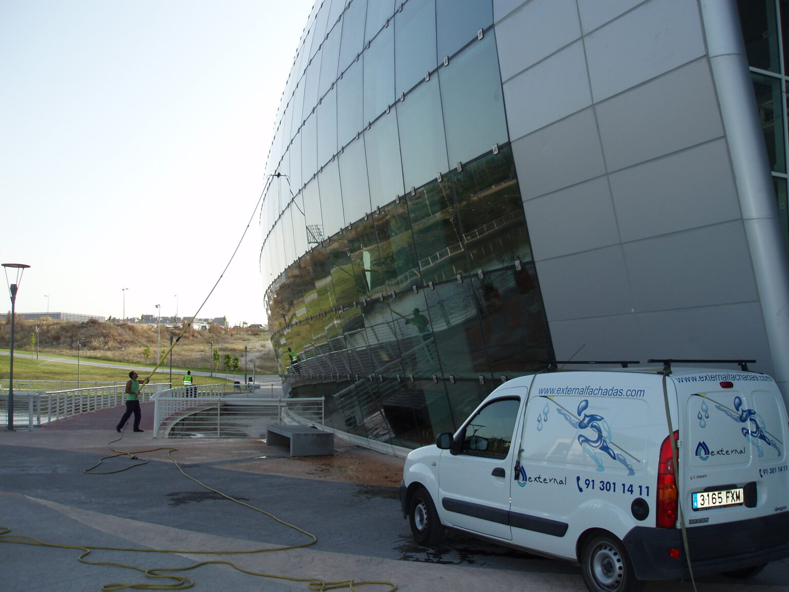 Operario de EXTERNAL FACHADAS realizando la limpieza de cristales de una fachada acristalada con pértiga telescópica en un edificio de Madrid.