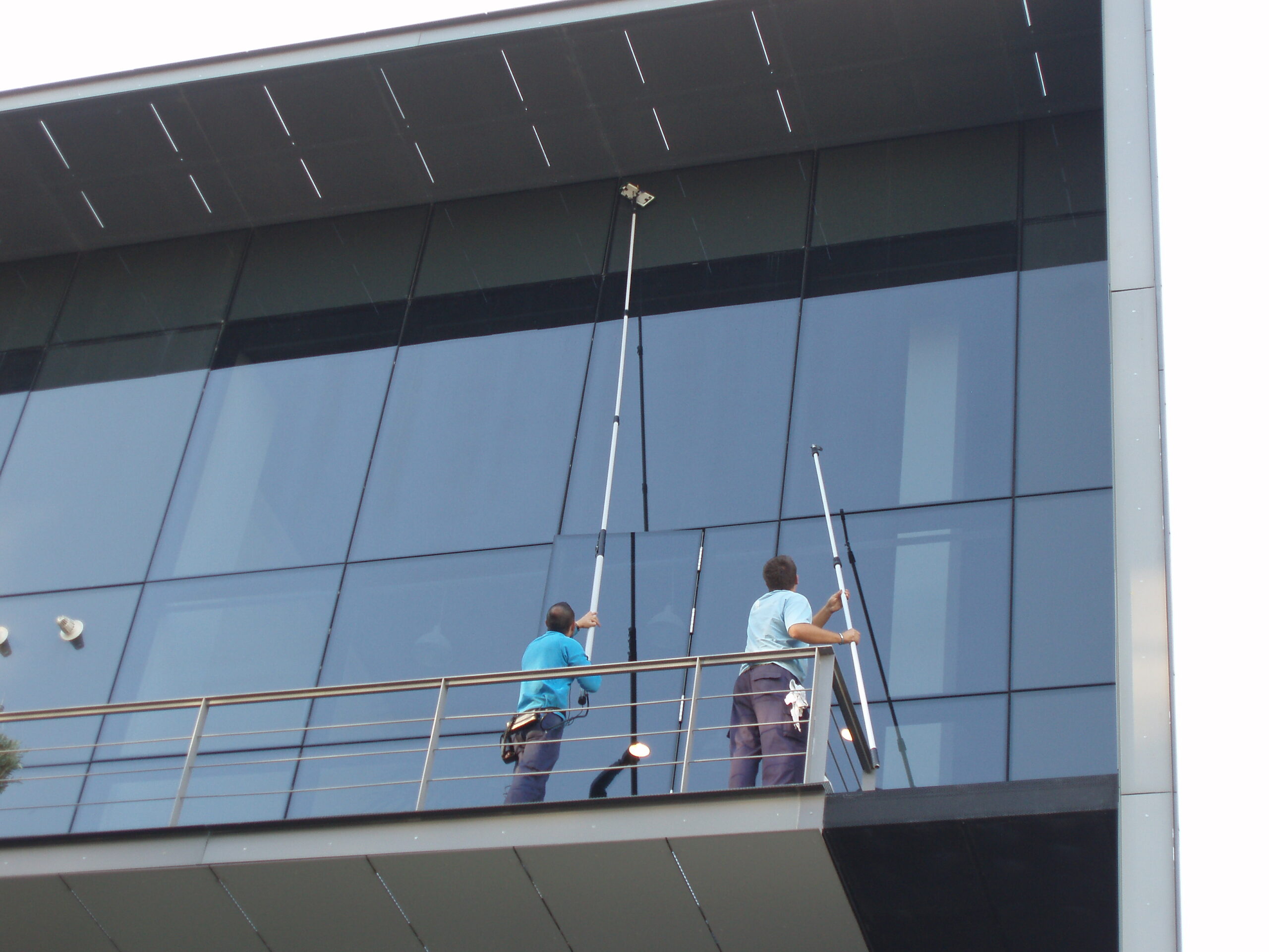 Técnicos de EXTERNAL FACHADAS realizando la limpieza de cristales de difícil acceso con pértiga telescópica en un edificio de oficinas en Madrid.
